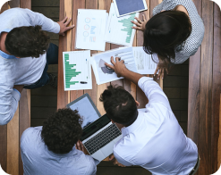 A group of people sitting around a table with papers and laptops.