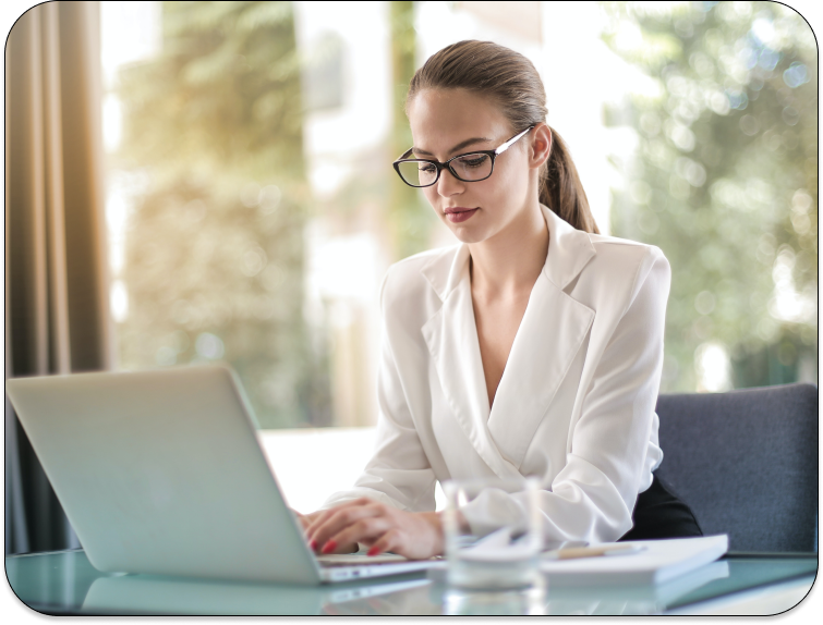 A woman in glasses is working on a laptop.